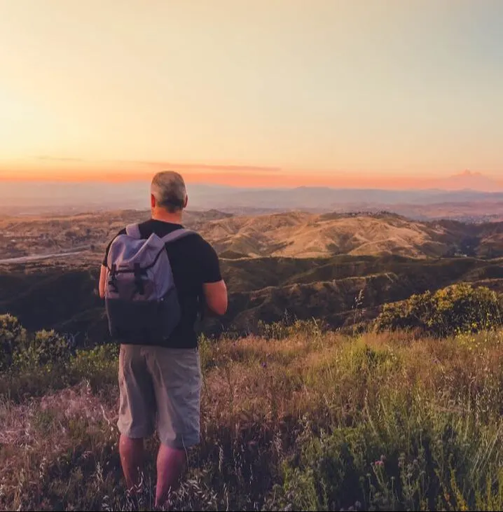 A man with a backpack looking out over the hills at sunset