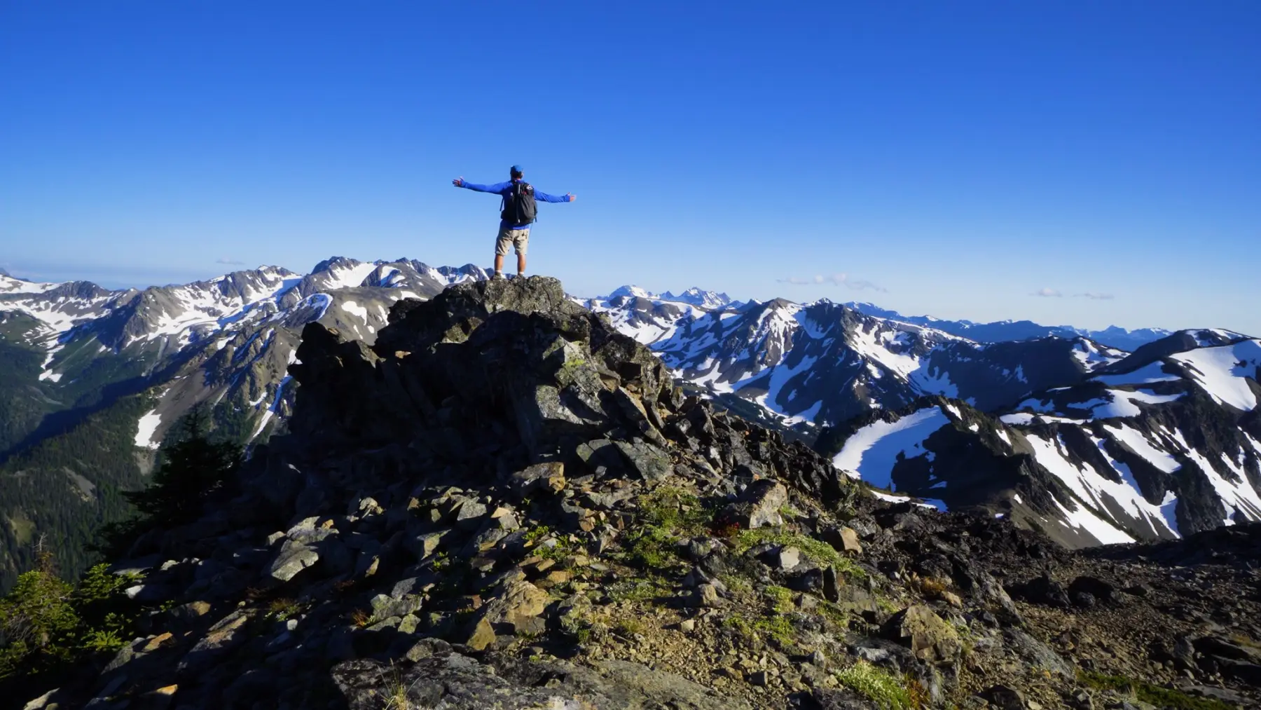 A hiker with arms outstretched on a peak in the Olympic Mountains